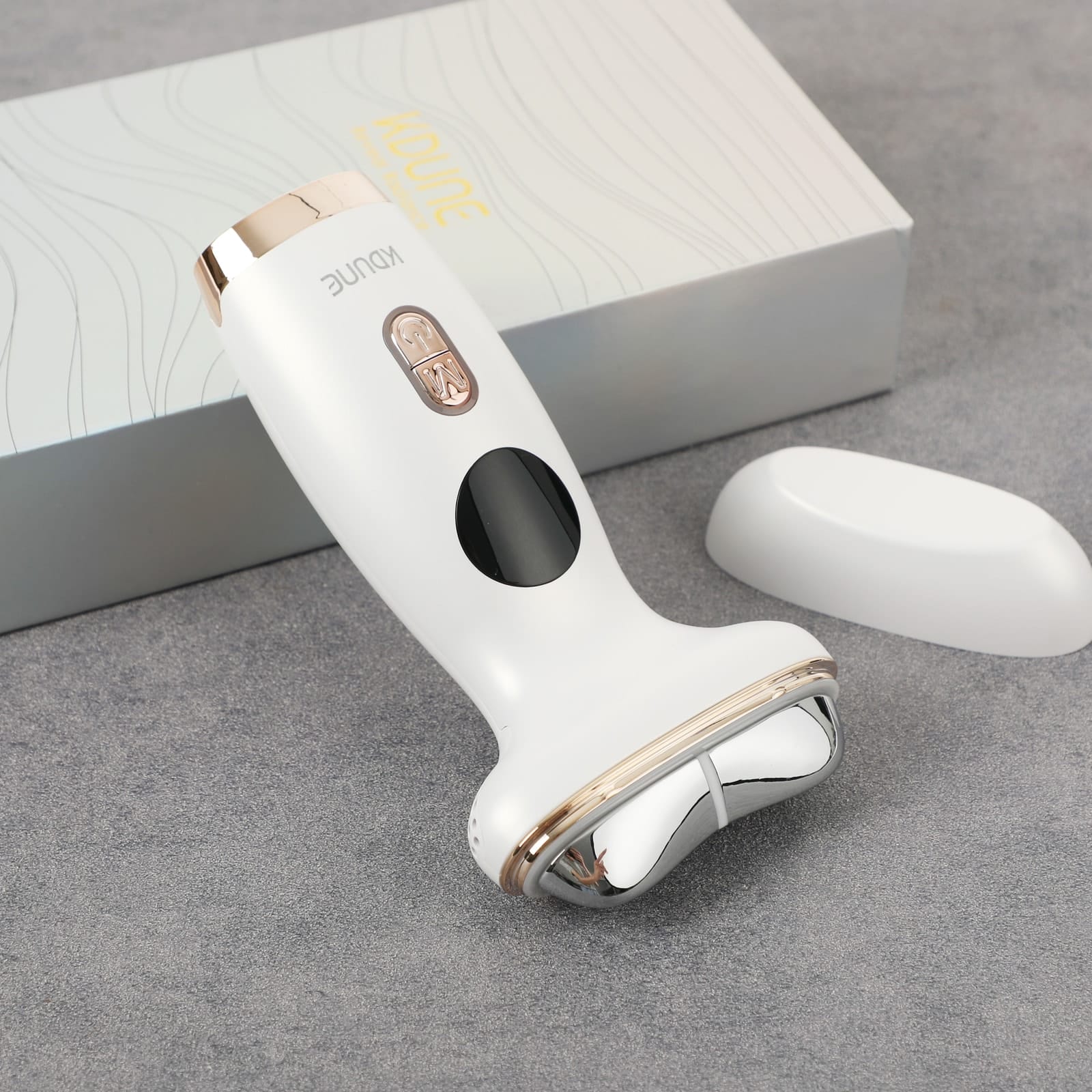 Close view of the Kdune 7-in-1 treatment head and its metal plate against a grey backdrop.